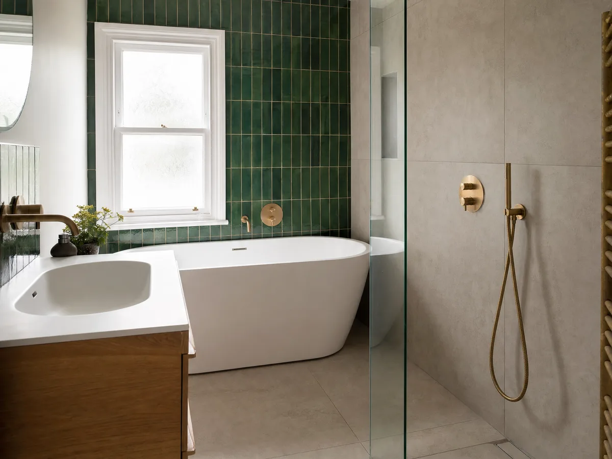A renovated bathroom with a freestanding bath under a sash window, green glazed tiles and a walk-in shower