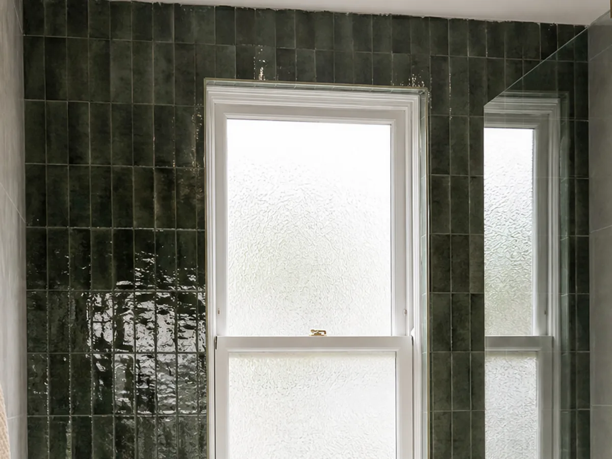 Deep green glazed vertical wall tiles around a white sash window